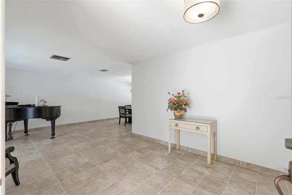 A room with light tile flooring, a black grand piano, and a small console table — 707 KNOLLWOOD DRIVE, LARGO, FL
