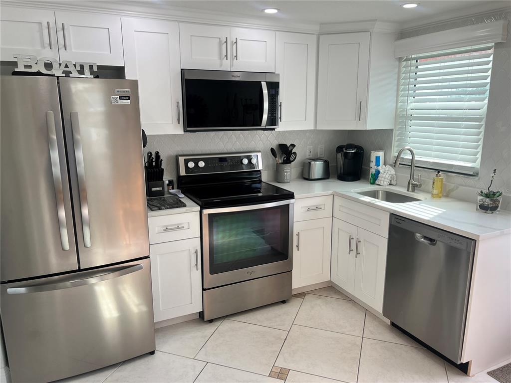 A kitchen features white cabinets, stainless steel appliances, a tiled backsplash, and light-colored floor tiles — 6154 MIDNIGHT PASS ROAD UNIT B16, SARASOTA, FL
