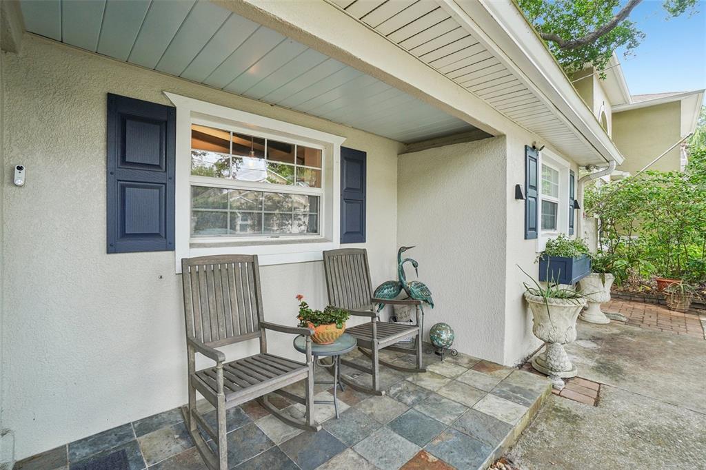 A covered front porch features two wooden rocking chairs, a small table, and tiled flooring — 3218 W OAKELLAR AVENUE, TAMPA, FL