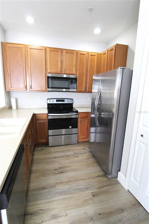 A kitchen features wood cabinets, stainless steel appliances, and light-colored countertops over wood-look flooring — 3475 PARKRIDGE CIRCLE UNIT 17-202, SARASOTA, FL