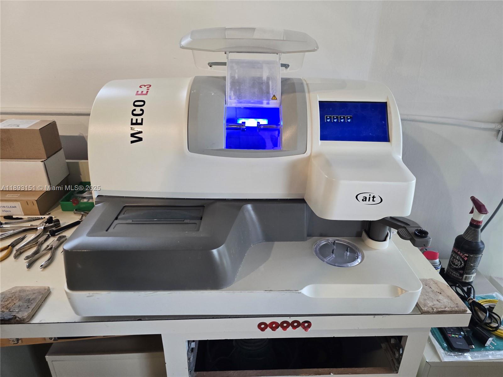 A Weco E.3 optical lens edger sits on a white workbench in a workspace — 2100 Coral Way, Coral Gables FL 33145, CORAL GABLES, FL