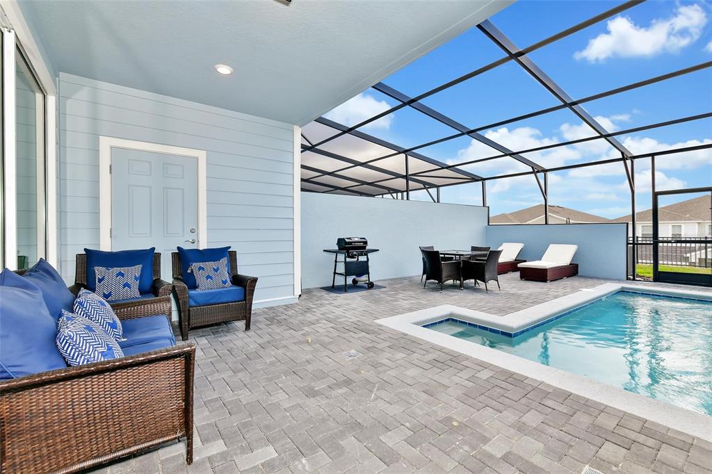 A covered patio features a pool, outdoor furniture, and a grill within a screened enclosure — 3721 PACIFIC LANE, DAVENPORT, FL