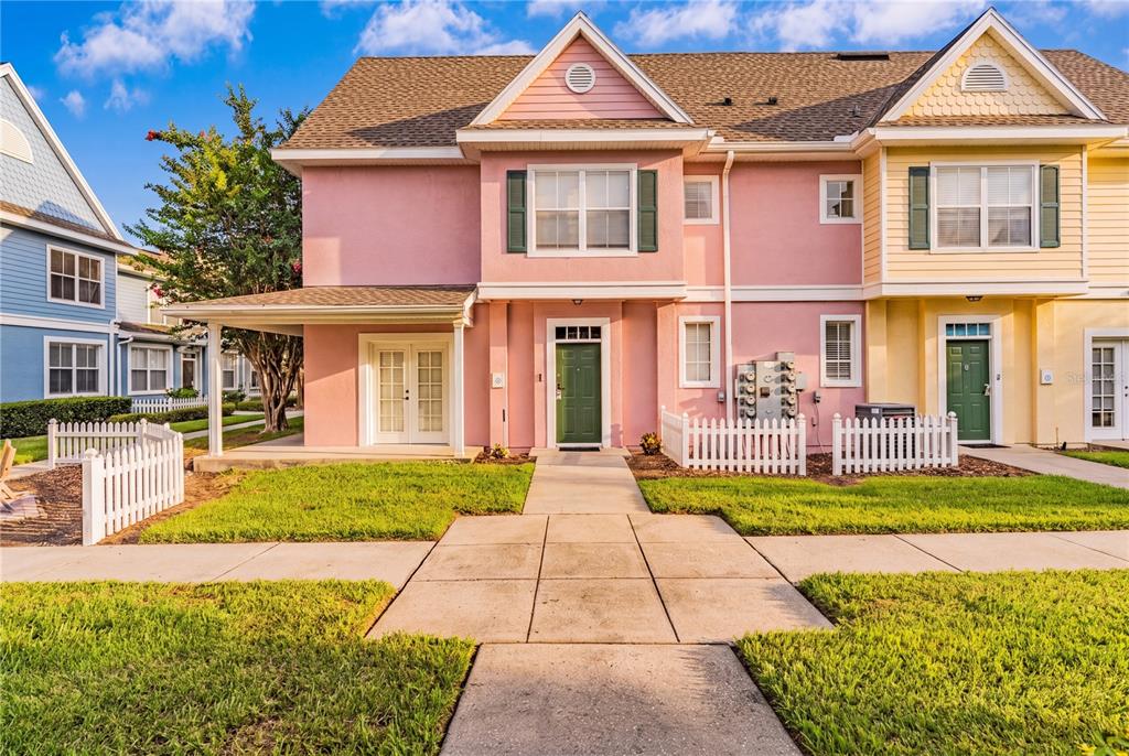 A pink and yellow multi-family townhouse exterior with white picket fences and green front doors — 4006 SAN GALLO DRIVE UNIT 108, KISSIMMEE, FL