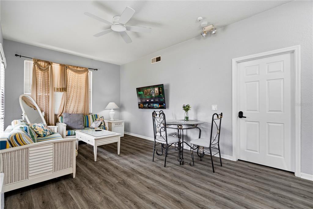 A living room features gray wood-look flooring, a ceiling fan, a wall-mounted television, and furniture — 4006 SAN GALLO DRIVE UNIT 108, KISSIMMEE, FL