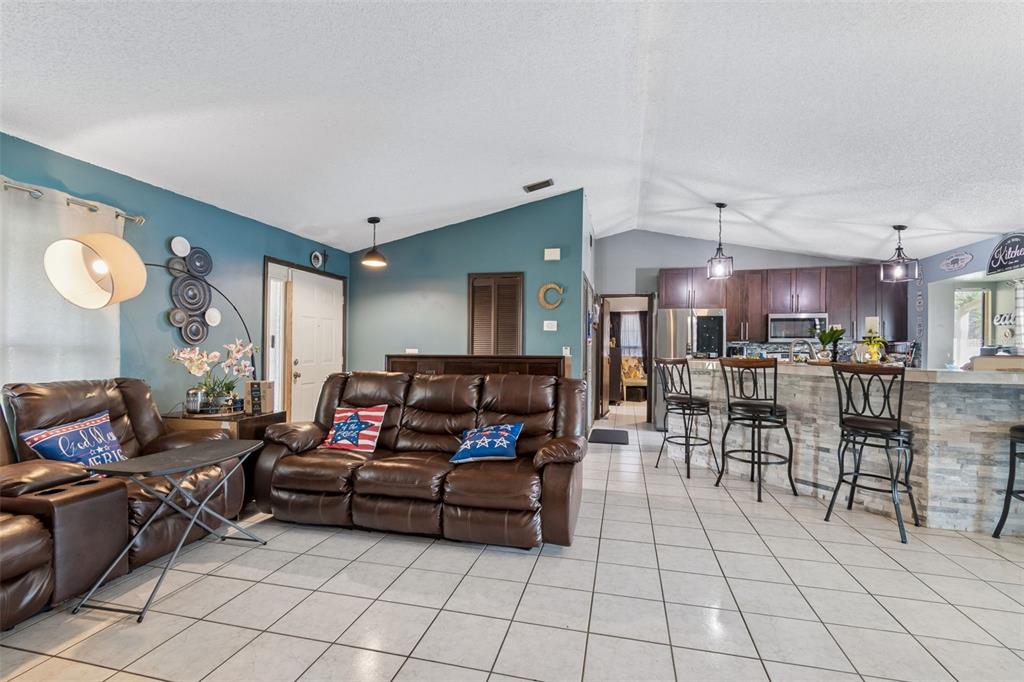A living room with tile floors, a brown leather sofa, and an open kitchen area — 10326 OUT ISLAND DRIVE, TAMPA, FL