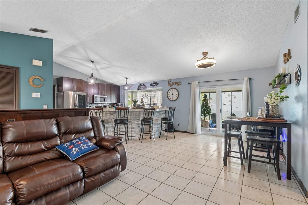 A living room with a brown leather sofa, tile flooring, and an open kitchen area — 10326 OUT ISLAND DRIVE, TAMPA, FL