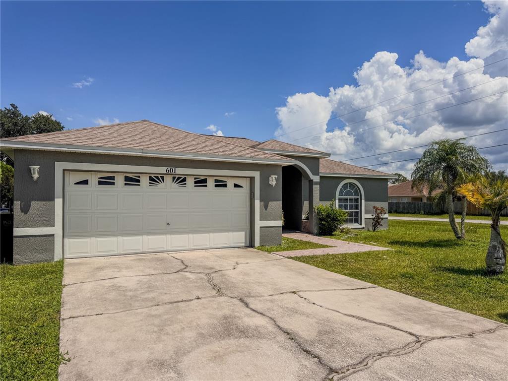 A single-story house with a gray stucco exterior, a two-car garage, and a concrete driveway — 601 BOBCAT LANE, KISSIMMEE, FL