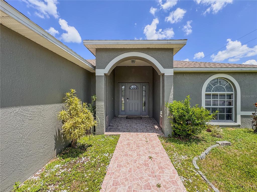 The exterior of a house features a tiled walkway leading to a covered arched entryway — 601 BOBCAT LANE, KISSIMMEE, FL
