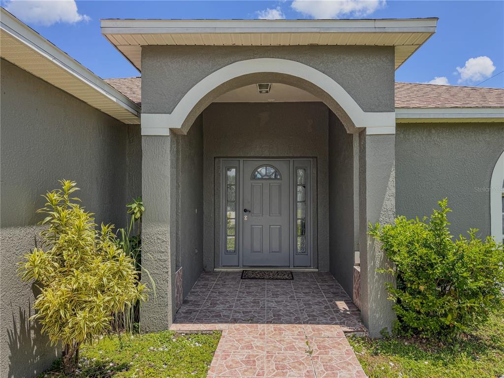 A gray front door with sidelights is framed by a covered entryway with tiled flooring — 601 BOBCAT LANE, KISSIMMEE, FL