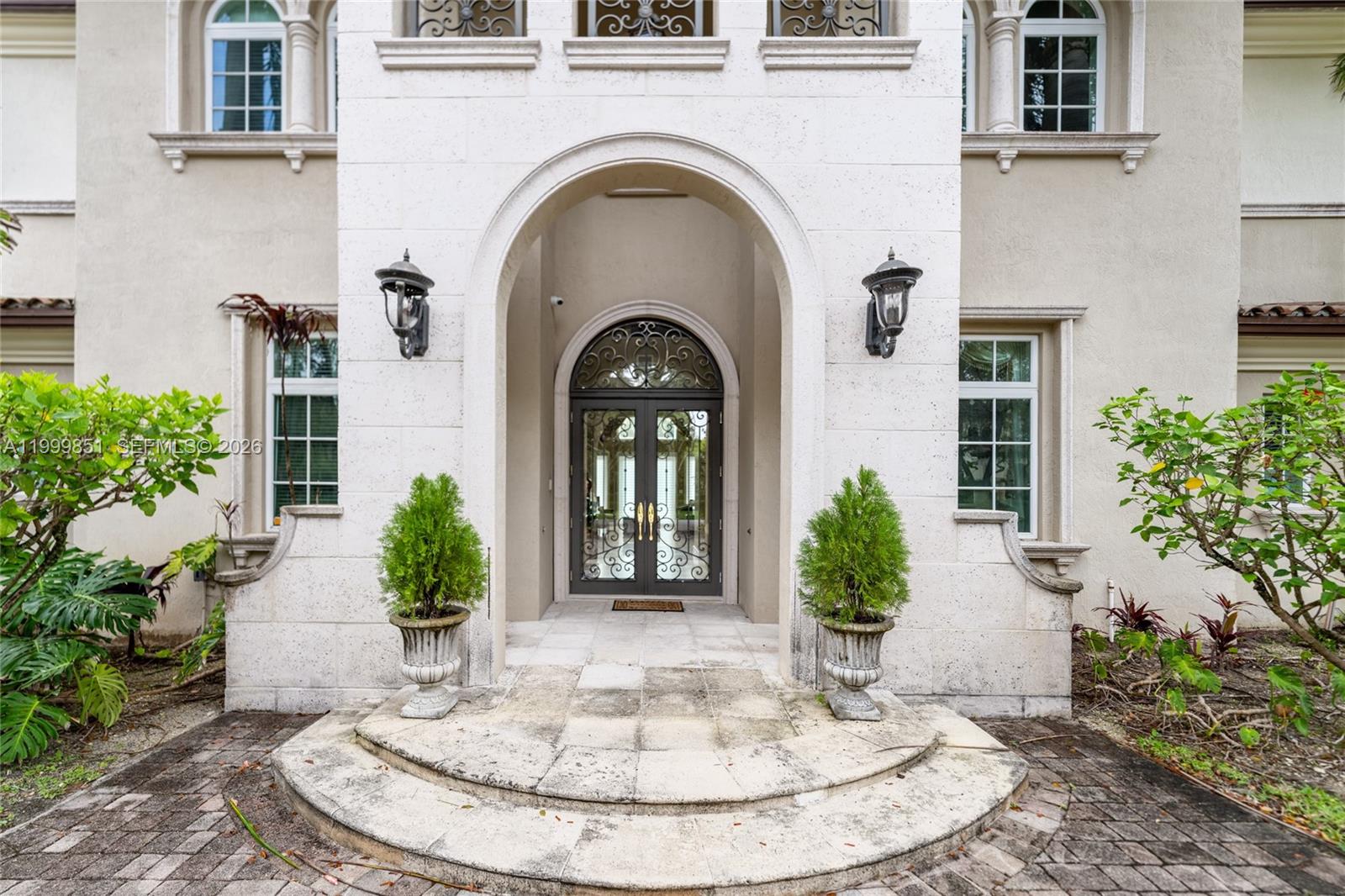 The exterior of a house features an arched entryway with double glass doors and planters — 12101 Moss Ranch Rd, Pinecrest FL 33156, PINECREST, FL