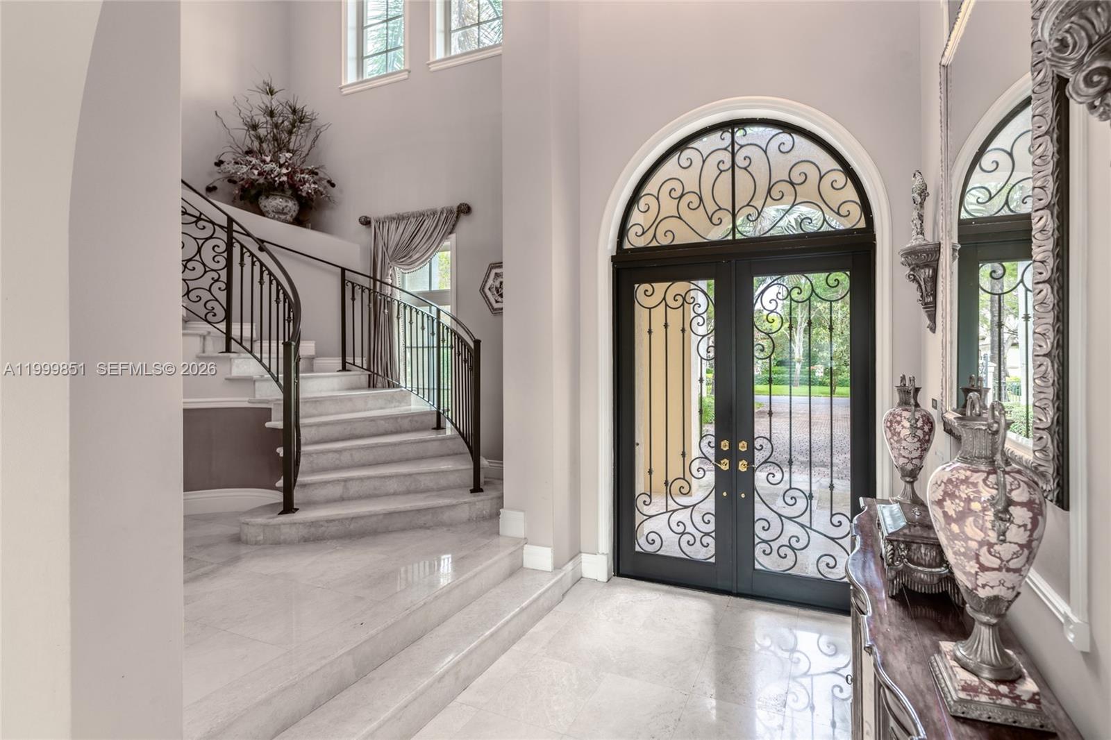 A grand foyer features a curved marble staircase, wrought iron railings, and arched double doors — 12101 Moss Ranch Rd, Pinecrest FL 33156, PINECREST, FL