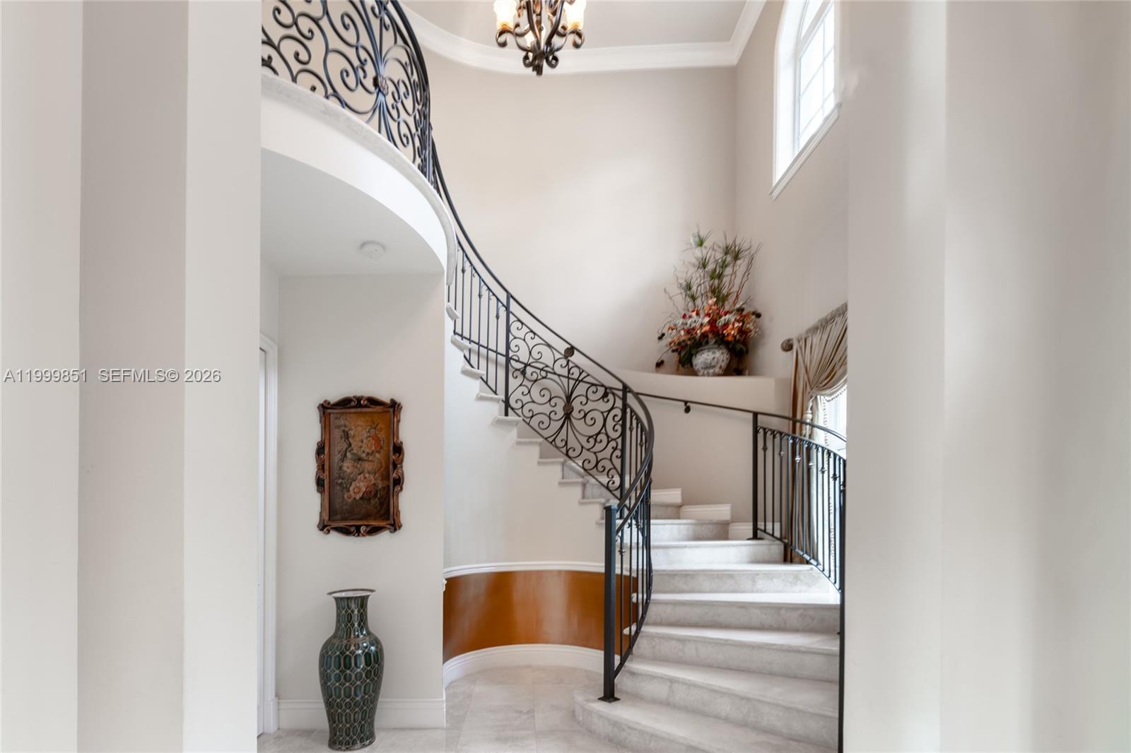 A curved staircase with wrought iron railings stands in a bright, high-ceilinged foyer — 12101 Moss Ranch Rd, Pinecrest FL 33156, PINECREST, FL
