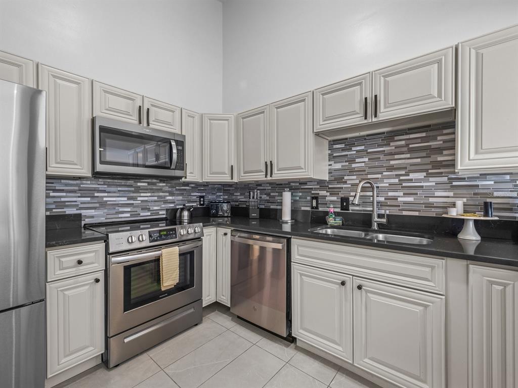 A kitchen with stainless steel appliances, off-white cabinets, and a multi-colored glass tile backsplash — 4700 SW ARCHER ROAD UNIT 2, GAINESVILLE, FL