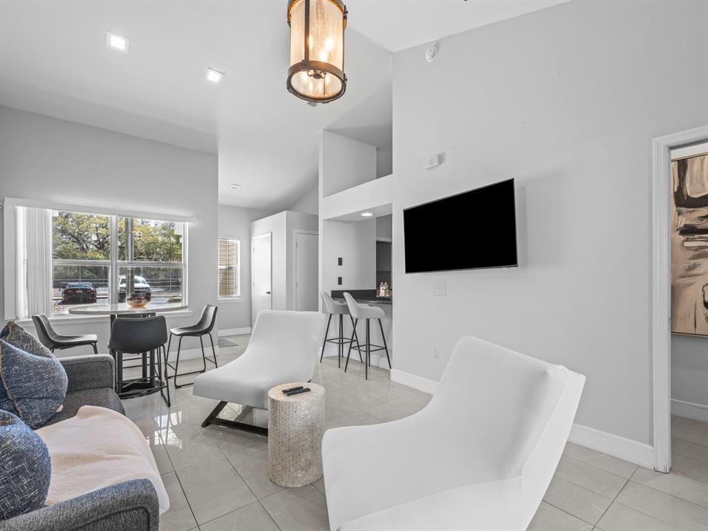 A living room features white chairs, a gray sofa, a dining area, and a wall-mounted television — 4700 SW ARCHER ROAD UNIT 2, GAINESVILLE, FL
