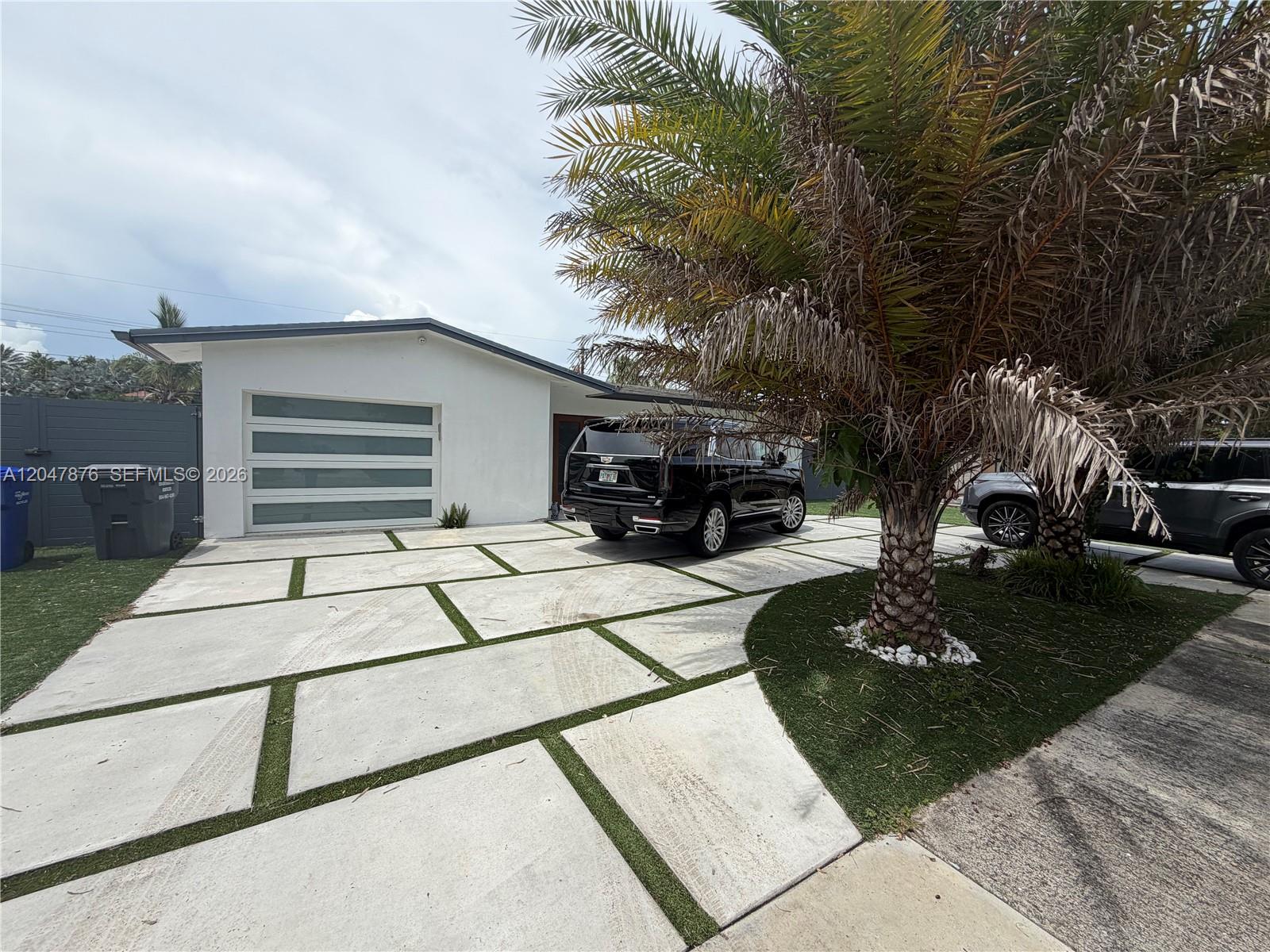 A white house with a modern garage door and a paved driveway featuring grass strips — 7525 Roosevelt St, Hollywood FL 33024, HOLLYWOOD, FL