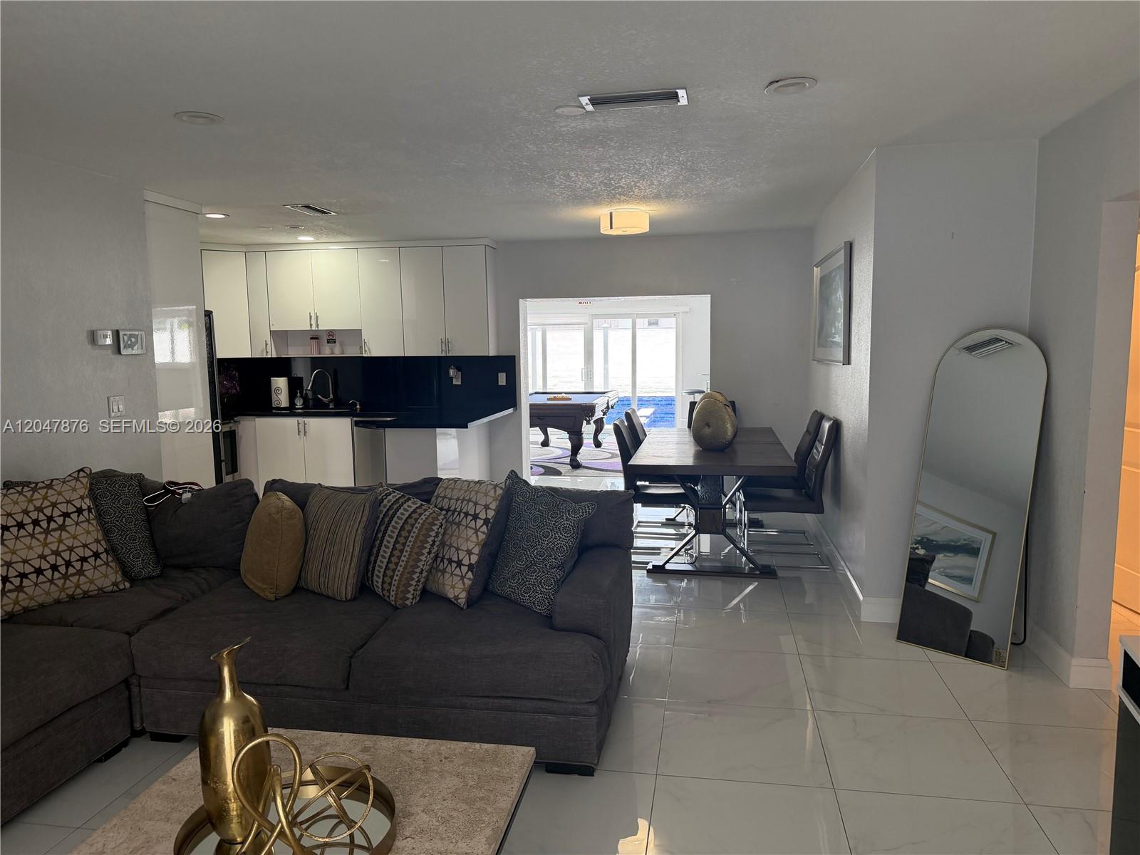 An open-concept living and dining area features a gray sectional, kitchen, and pool view — 7525 Roosevelt St, Hollywood FL 33024, HOLLYWOOD, FL