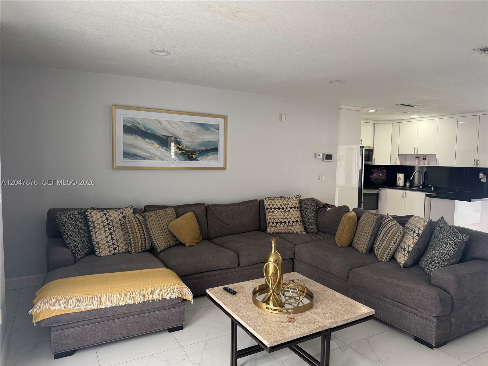 A living room features a large gray sectional sofa, a stone coffee table, and an open kitchen — 7525 Roosevelt St, Hollywood FL 33024, HOLLYWOOD, FL