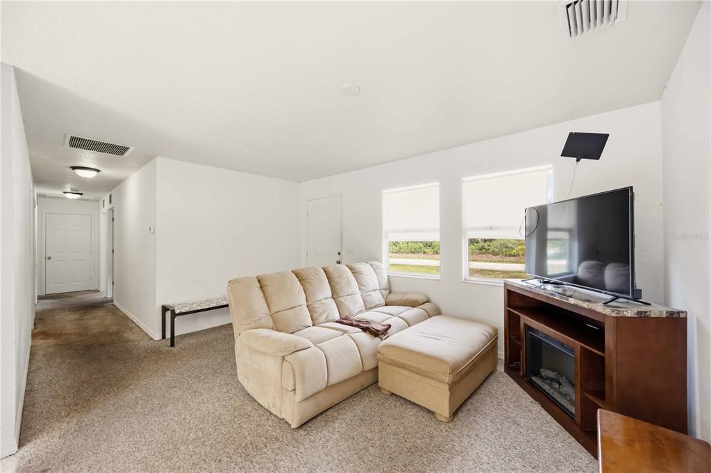 A living room features beige carpet, a tan sofa with an ottoman, and a fireplace console — 105 BISCAYNE DRIVE, PORT CHARLOTTE, FL