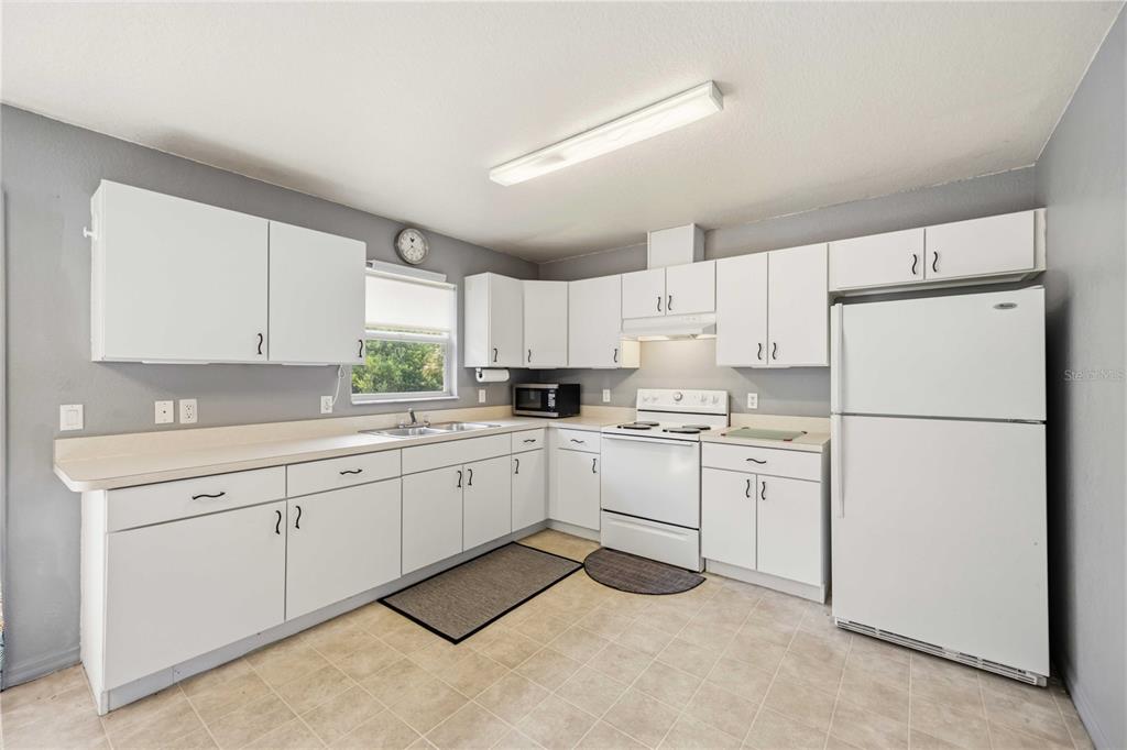 A kitchen features white cabinetry, a white stove, a white refrigerator, and light-colored tile flooring — 105 BISCAYNE DRIVE, PORT CHARLOTTE, FL