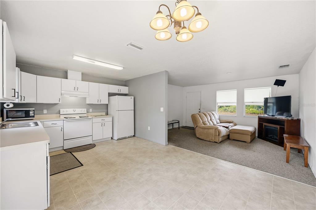 An open-concept kitchen with white cabinets and tile flooring flows into a carpeted living area — 105 BISCAYNE DRIVE, PORT CHARLOTTE, FL