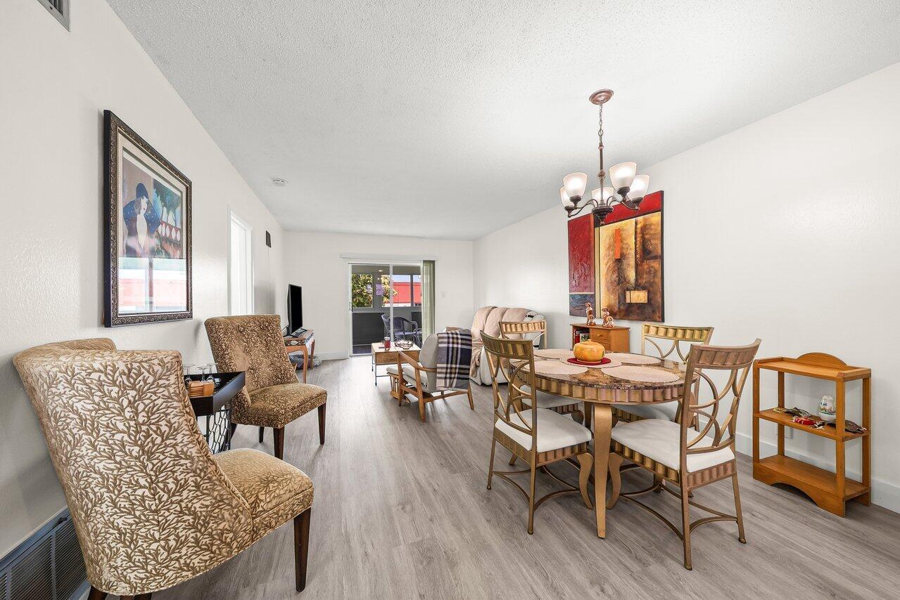 A dining and living area features light wood-look flooring, a chandelier, and a sliding door — 1117 Lake Terrace # 207, Boynton Beach FL 33426, BOYNTON BEACH, FL
