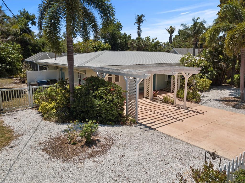 A single-story house with a metal roof, a wooden pergola, and a gravel driveway — 7860 HOLIDAY DRIVE, SARASOTA, FL
