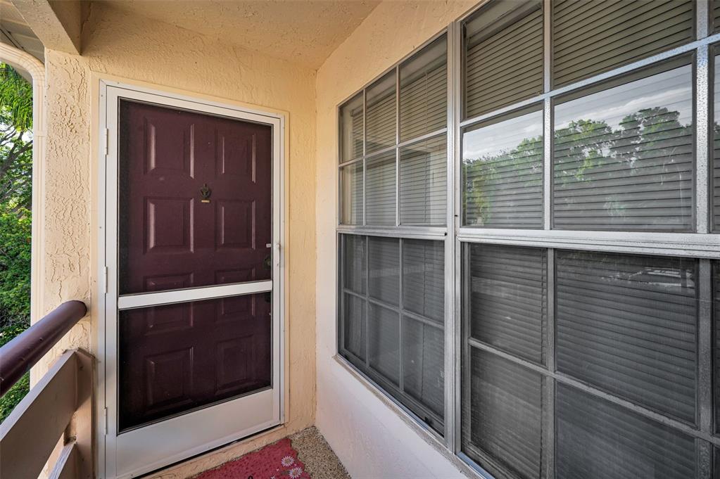 A dark brown front door with a white storm door sits beside large grid windows — 7837 HARDWICK DRIVE UNIT 327, NEW PORT RICHEY, FL