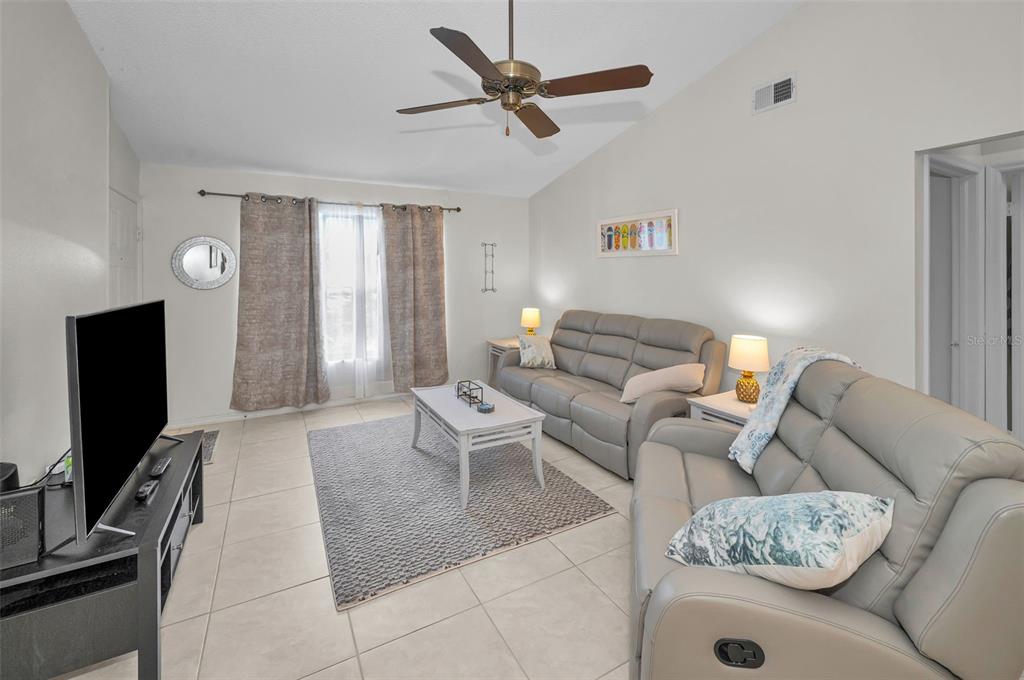 A living room features light tile floors, gray leather sofas, a coffee table, and ceiling fan — 7837 HARDWICK DRIVE UNIT 327, NEW PORT RICHEY, FL