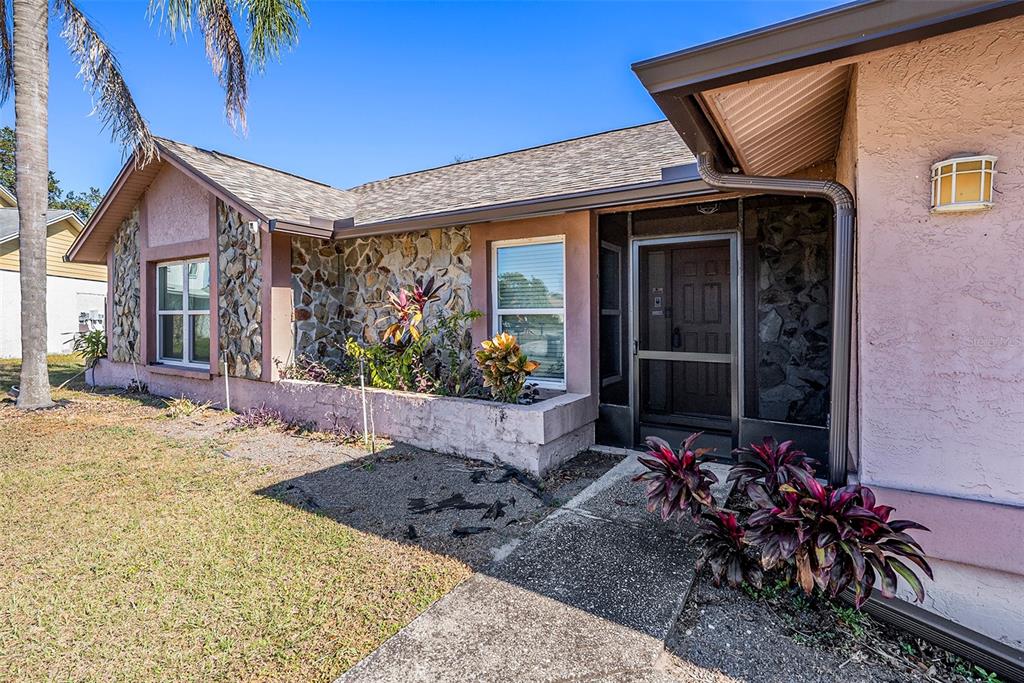 A pink house exterior features a stone facade, a screened front door, and landscaping — 1606 DUSTY ROSE LANE, BRANDON, FL