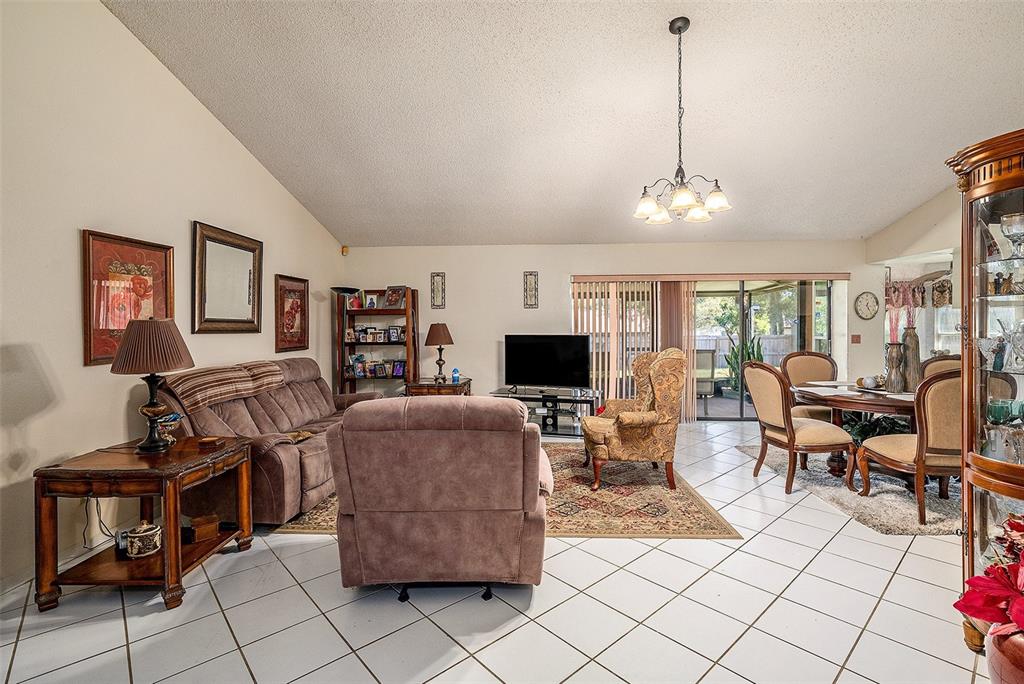 A living and dining area with tile floors, a vaulted ceiling, and a glass chandelier — 1606 DUSTY ROSE LANE, BRANDON, FL