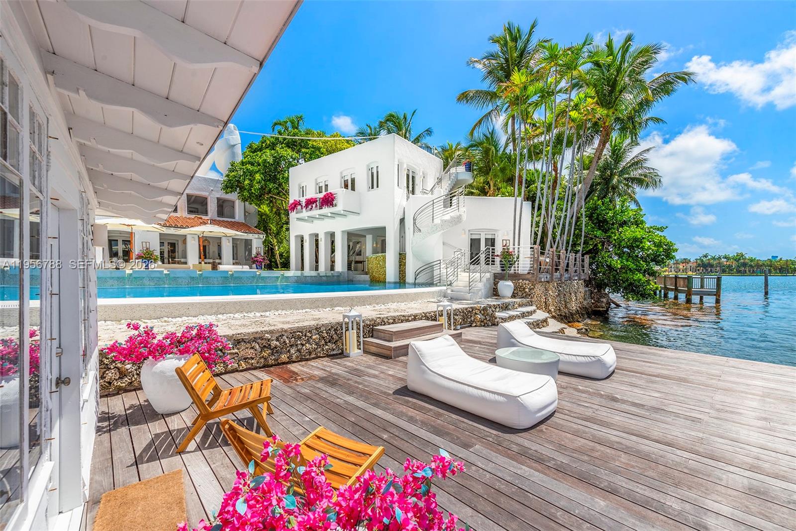 A wooden deck with lounge chairs overlooks a swimming pool and a white waterfront house — 24 S Hibiscus Dr, Miami Beach FL 33139, MIAMI BEACH, FL