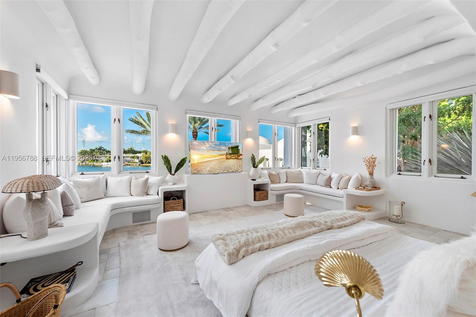 This bright bedroom features built-in white seating, exposed ceiling beams, and large windows overlooking water — 24 S Hibiscus Dr, Miami Beach FL 33139, MIAMI BEACH, FL