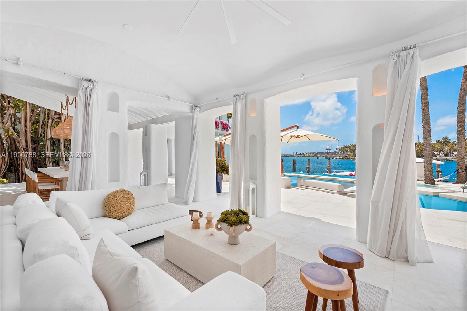 A bright, white living room opens to a patio with a pool and waterfront view — 24 S Hibiscus Dr, Miami Beach FL 33139, MIAMI BEACH, FL