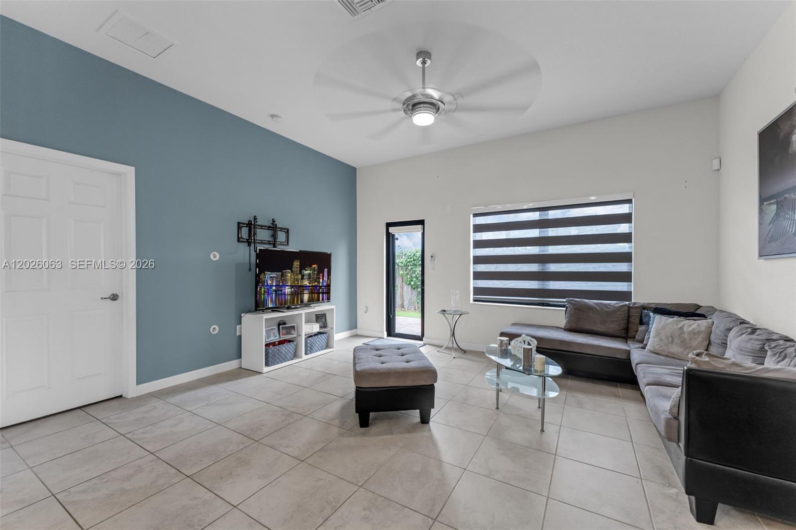 A living room features a blue accent wall, tile flooring, a ceiling fan, and furniture — 134 NE 23rd Ter, Homestead FL 33033, HOMESTEAD, FL