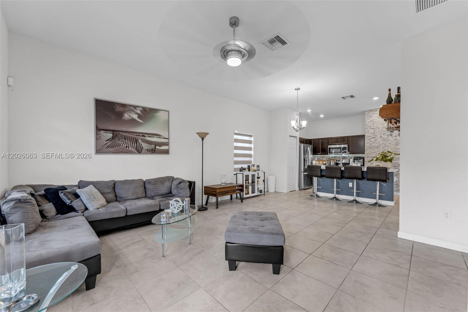 An open-concept living room features a grey sectional sofa, tile flooring, and a kitchen island — 134 NE 23rd Ter, Homestead FL 33033, HOMESTEAD, FL