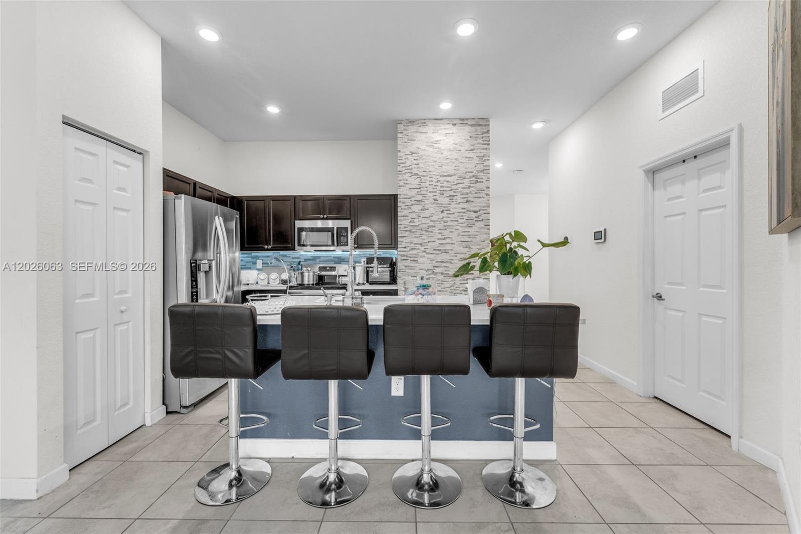A kitchen features a blue island with four bar stools, dark cabinets, and stone accents — 134 NE 23rd Ter, Homestead FL 33033, HOMESTEAD, FL