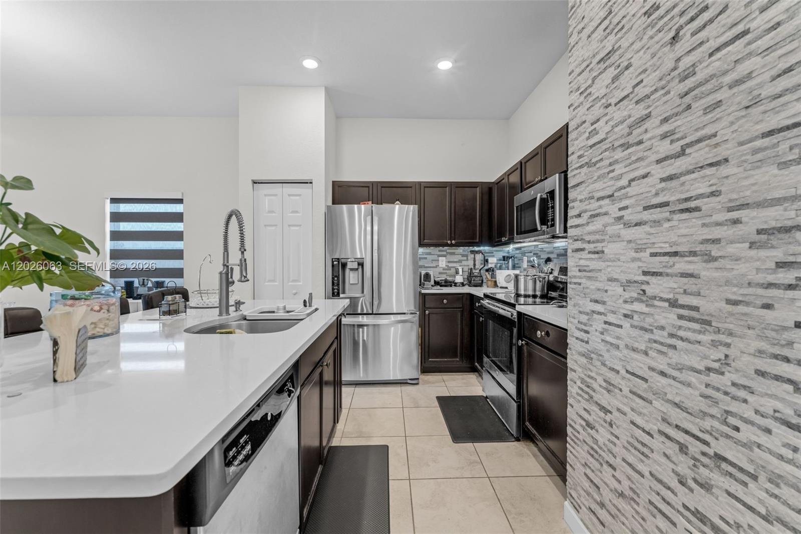 A kitchen features dark wood cabinets, stainless steel appliances, white countertops, and a stone-tiled wall — 134 NE 23rd Ter, Homestead FL 33033, HOMESTEAD, FL