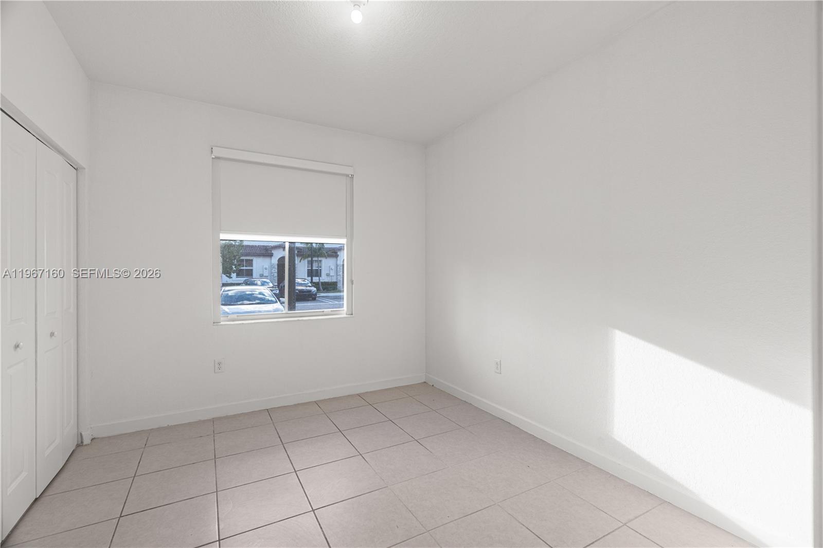 A small, empty room features white walls, light-colored tile flooring, and a single window — 12121 NW 23rd Ct, Miami FL 33167, MIAMI, FL