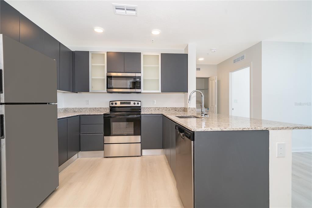 A kitchen features dark gray cabinets, stainless steel appliances, and speckled granite countertops — 5579 MILLENIA PARK BLVD UNIT 521, ORLANDO, FL