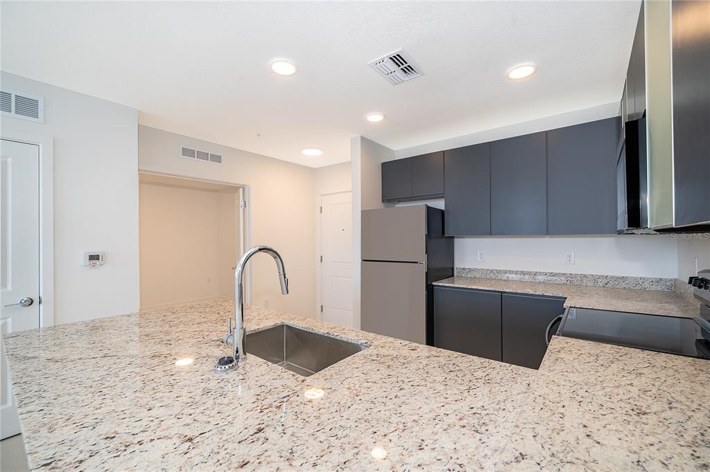 A kitchen features granite countertops, dark gray cabinets, a stainless steel refrigerator, and an island — 5579 MILLENIA PARK BLVD UNIT 521, ORLANDO, FL