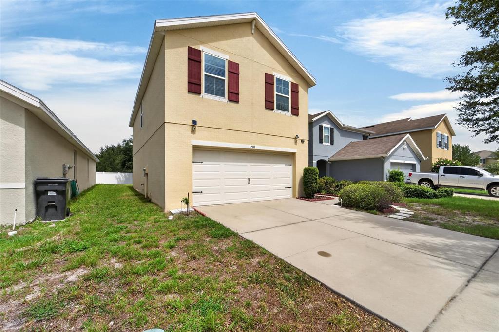 A two-story house with a beige stucco exterior, a two-car garage, and red shutters — 12111 FAWN BRINDLE STREET, RIVERVIEW, FL