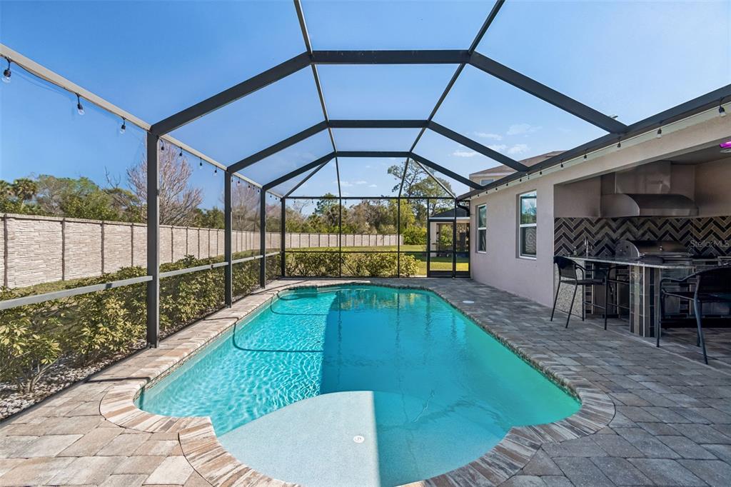 A screened-in patio features a swimming pool, stone pavers, and an outdoor kitchen area — 7432 47TH AVENUE CIRCLE E, BRADENTON, FL