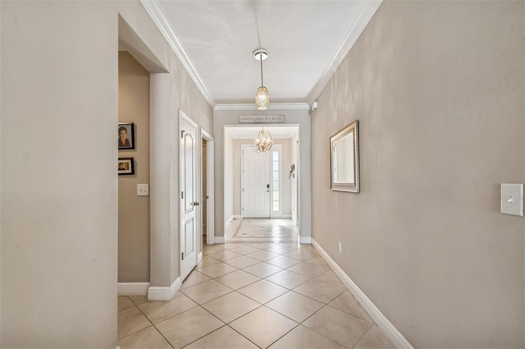 A tiled hallway leads to a front door with a chandelier and crown molding — 7432 47TH AVENUE CIRCLE E, BRADENTON, FL