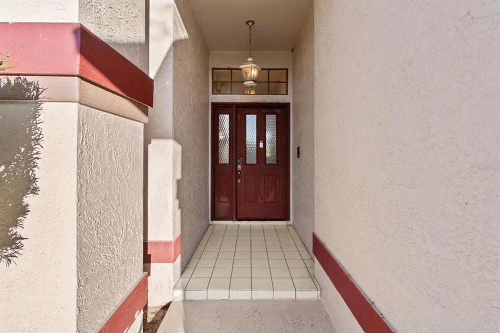 A covered entryway features a red front door with glass panels and tiled flooring — 10431 36TH STREET N, CLEARWATER, FL