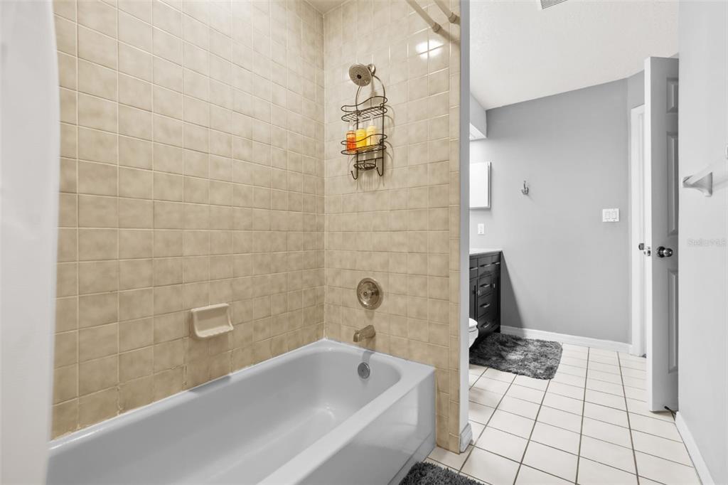 A bathroom features a beige tiled bathtub surround, a shower caddy, and white floor tiles — 10431 36TH STREET N, CLEARWATER, FL