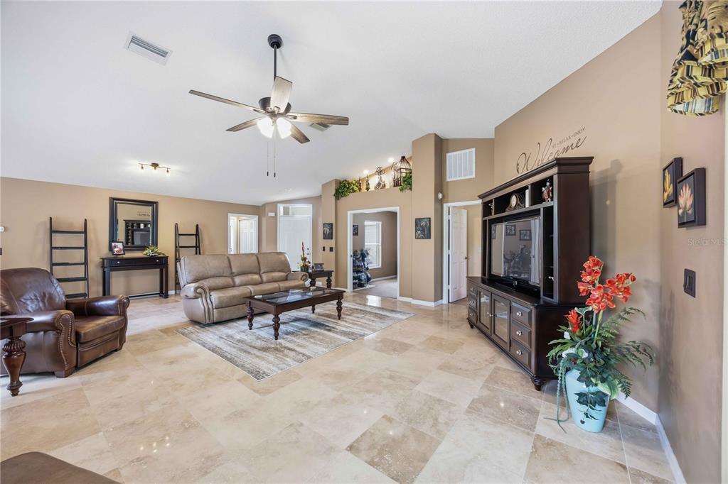 A spacious living room features beige tile flooring, a ceiling fan, and a large entertainment center — 1082 TEQUESTA TRAIL, LAKE WALES, FL
