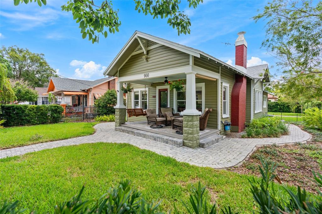 A green bungalow with a red brick chimney and a covered front porch with seating — 900 E PINE STREET, ORLANDO, FL