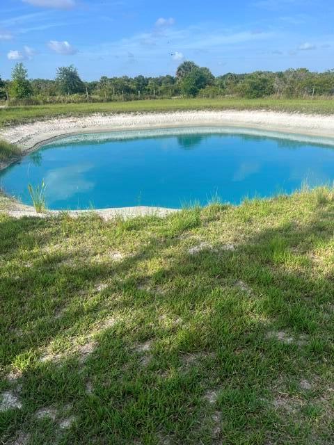 A bright blue pond is surrounded by a grassy bank and a line of trees — 20641 NW 302nd Street, Okeechobee FL 34972, OKEECHOBEE, FL