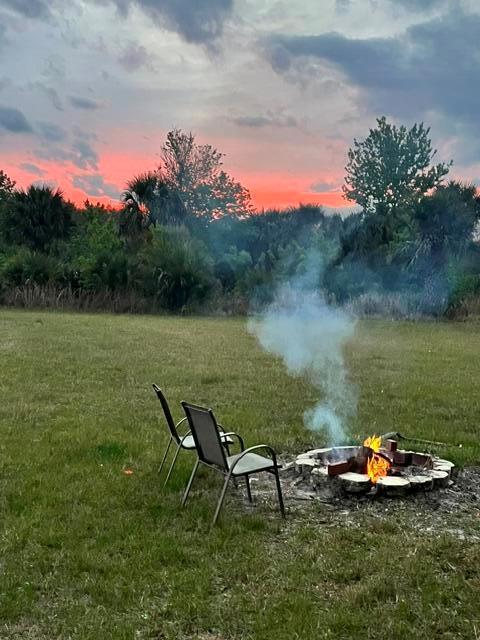 Two outdoor chairs sit on a grassy lawn next to a small fire pit at sunset — 20641 NW 302nd Street, Okeechobee FL 34972, OKEECHOBEE, FL