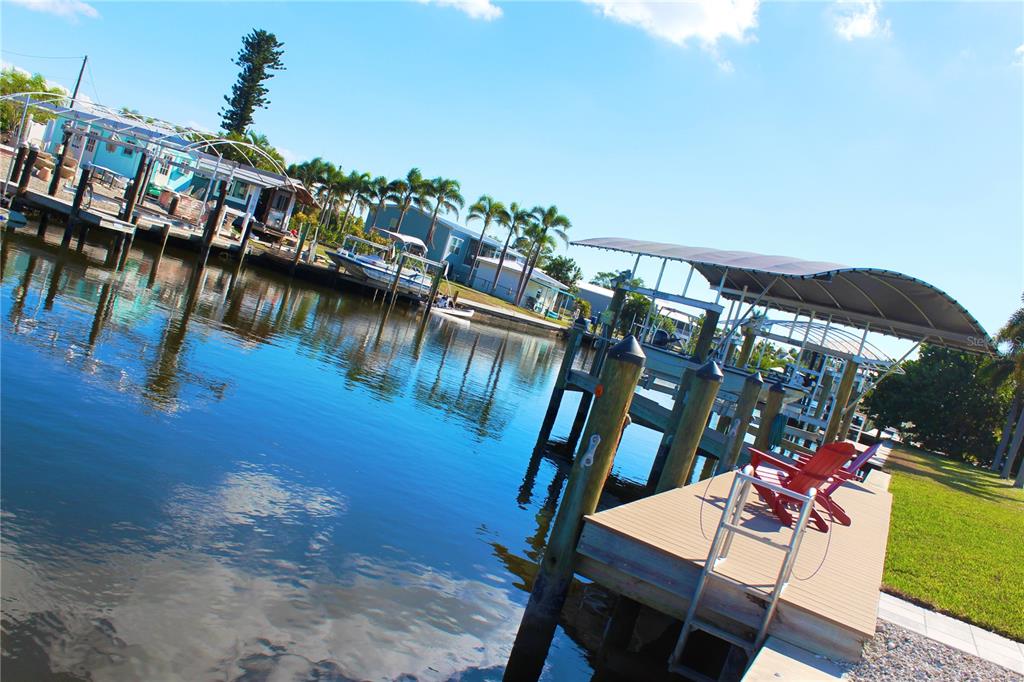 A wooden boat dock with a covered slip and red chairs sits along a canal — 2744 SANDERLING COURT, ST JAMES CITY, FL